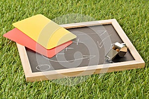 Soccer sports referee chrome whistle with game strategy drawing blackboard and yellow and red referee cards on grass background