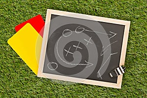 Soccer sports referee chrome whistle with game strategy drawing blackboard and yellow and red referee cards on grass background