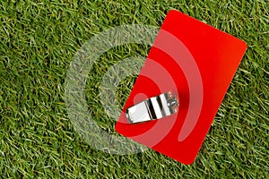 Soccer sports referee red card with whistle on grass background - penalty, foul or sports concept, top view flat lay from above