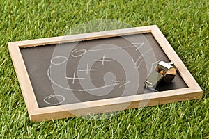 Soccer sports referee whistle with game strategy drawing blackboard on grass background - selective focus