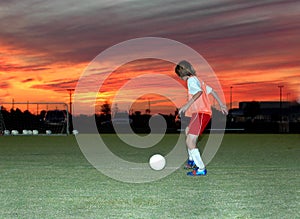 Un ragazzo pratica il calcio sotto un rosso del cielo al tramonto.