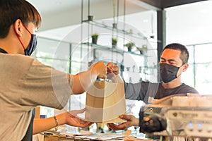 Social distance conceptual waiter giving takeaway bag to customer at cafe.