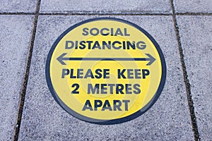 Social Distancing Please keep 2 metres apart yellow sign on pavement