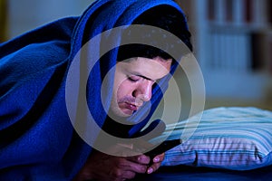 Social media addict men on bed not sleep because play smart phone, covering his head with a blue blanket, room