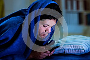 Social media addict men on bed not sleep because play smart phone, covering his head with a blue blanket, room