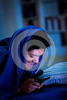 Social media addict men on bed not sleep because play smart phone, covering his head with a blue blanket, room
