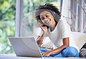 Social media at her fingertips. a young woman sitting at home using a laptop and wearing headphones.