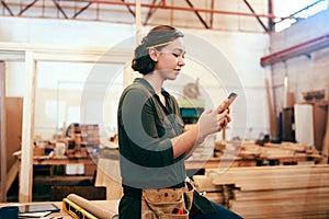 Social media is raving about our unique designs. a female carpenter using her cellphone in her workshop.