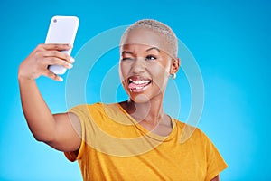 Social media, selfie and funny face with a black woman on blue background in studio to update her profile picture. Post