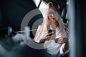 In the social medias. Smart businesswoman sits at backseat of the luxury car with black interior