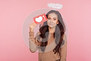 Social network Like button. Portrait of positive angelic young woman with halo over head holding internet Heart icon