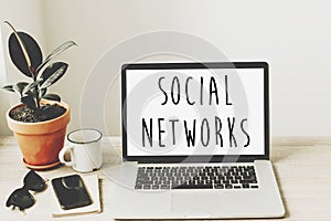 social networks text on laptop screen on wooden desktop with phone, notebook, coffee and plant. business workspace. global