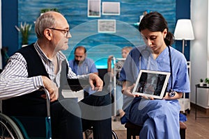 Social nurse worker explaining medical radiography using tablet computer to pensioner