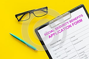 Social security benefits. Application form near pen and glasses on yellow background top view