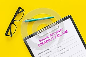 Social security. Disability claim form near pen and glasses on yellow background top view