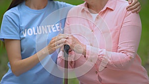 Social volunteer stroking old patient hand on walking stick, hospice support