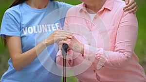 Social volunteer stroking old patient hand on walking stick, hospice support