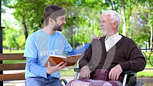 Social worker reading book for disabled pensioner, leisure in park, volunteering photo