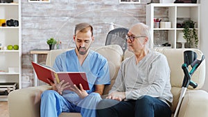 Social worker reading a book to an old disabled man in nursing home