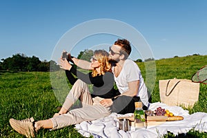 Social young couple taking a selfie during a picnic on a spring grassfield