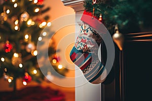 A sock with Christmas gifts near the fireplace on the background of a Christmas tree