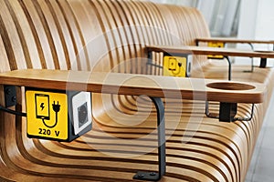 A socket with a device charging sign on a wooden bench at the airport.