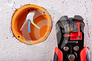 Socket in a raw wall with electric wires and electric insulation stripper. Repair of the electrical installation in the household