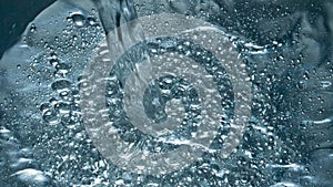 Soda blebs floating on the aqua surface closeup. Fizzy drink jet filling vessel