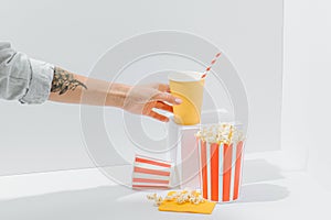 Soda cup with straw and popcorn in recyclable paper striped bucket held by woman