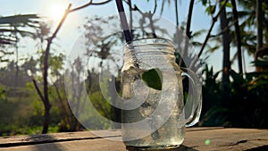 Soda water with lime in a glass jar on sunny evening on tropical island. Refreshing cocktail with ice. Thirsty on a hot