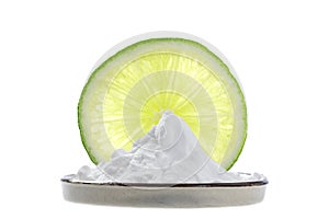 Sodium bicarbonate in a cup with a fine slice of lemon and two whole lime behind