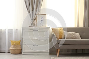 Sofa and chest of drawers near window with stylish curtains in living room. Interior design