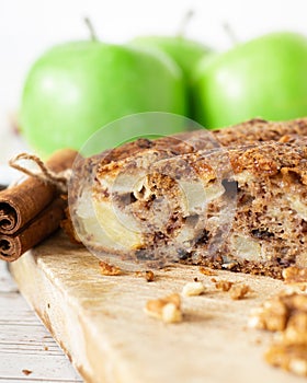 Soft apple cinnamon cake with walnuts on wooden table with crumbs and green Granny Smith apples in the background