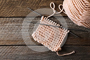 Soft beige yarn, knitting and metal needles on wooden table, flat lay. Space for text