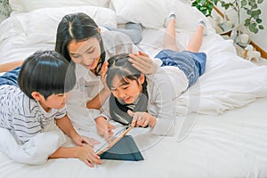 Soft blur of Asian mother and her children have fun with tablet in bedroom