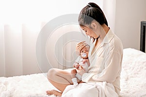 Soft blur image of beautiful Asian mother hold her newborn baby with baby teat on the white bed