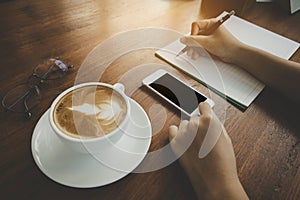 Soft and blurry,teenager hand, writing pencil holder, cell phone touching, Black space for text, Rounded vintage glasses and coffe