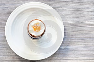 Soft-boiled brown egg in cup on plate on gray