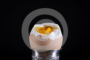 Soft boiled brown egg in eggcup on black background