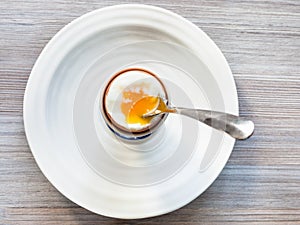 Soft-boiled brown egg with spoon in cup on plate
