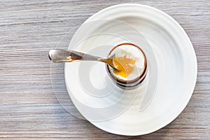 Soft-boiled brown egg with spoon on plate on gray