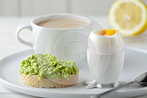 Soft-boiled egg with avocado sandwich and a cup of coffee with cream and on the table. European breakfast.