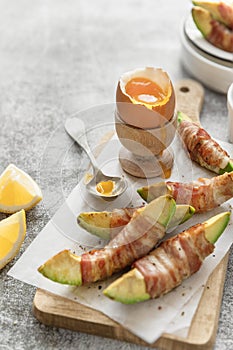 Soft boiled egg and bacon wrapped avocado peaces on cutting board