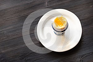 Soft-boiled egg in cup on plate on dark board