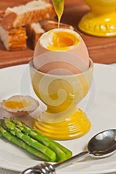 Soft boiled egg in a egg cup with the top cut off and an asparagus dipped into yolk