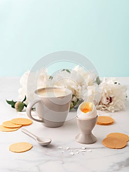 Soft-boiled egg with liquide orange yolk in ceramic egg cup, cup of coffee and thin crispy corn chips on background of