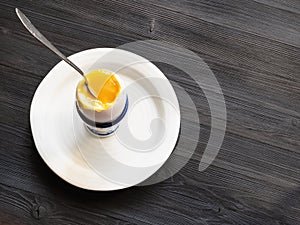 Soft-boiled egg with spoon in cup on plate on dark