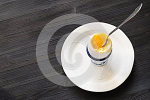 Soft-boiled egg with spoon on white plate on dark