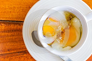 Soft boiled egg in white cup with pepper and spoon