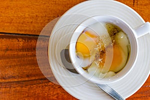 Soft boiled egg in white cup with pepper and spoon